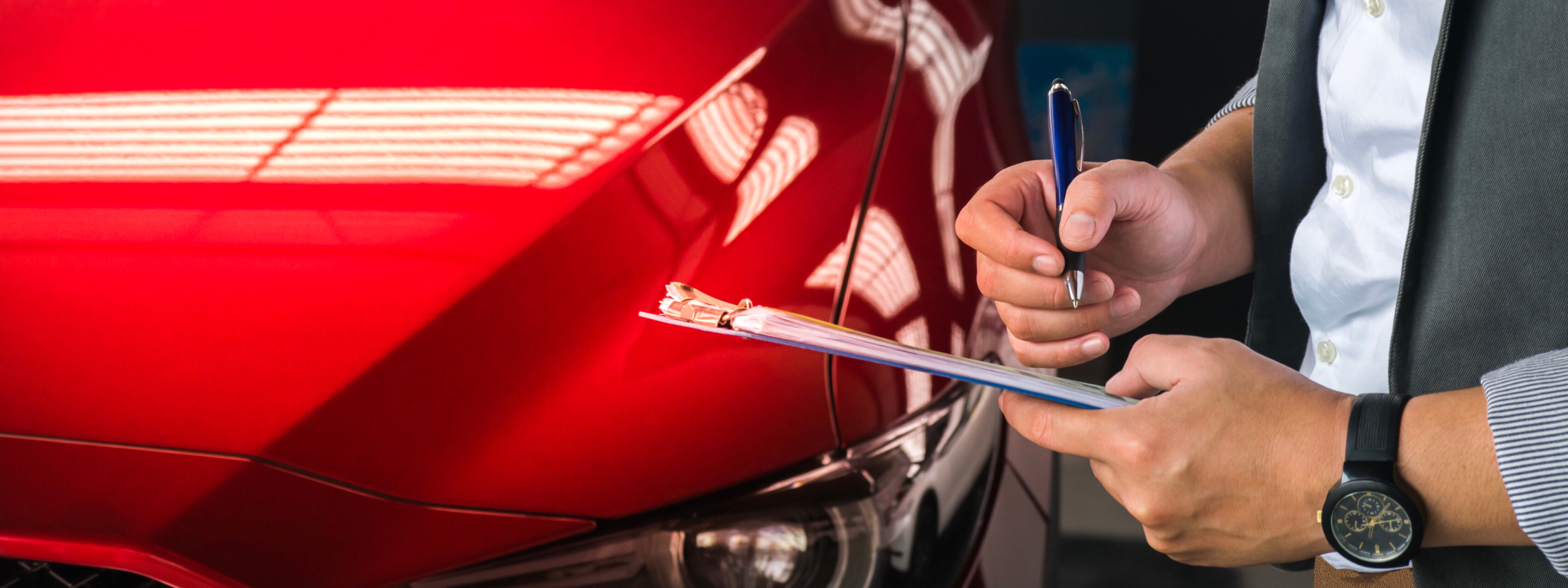 A man signing papers on a clipboard in front of a red car