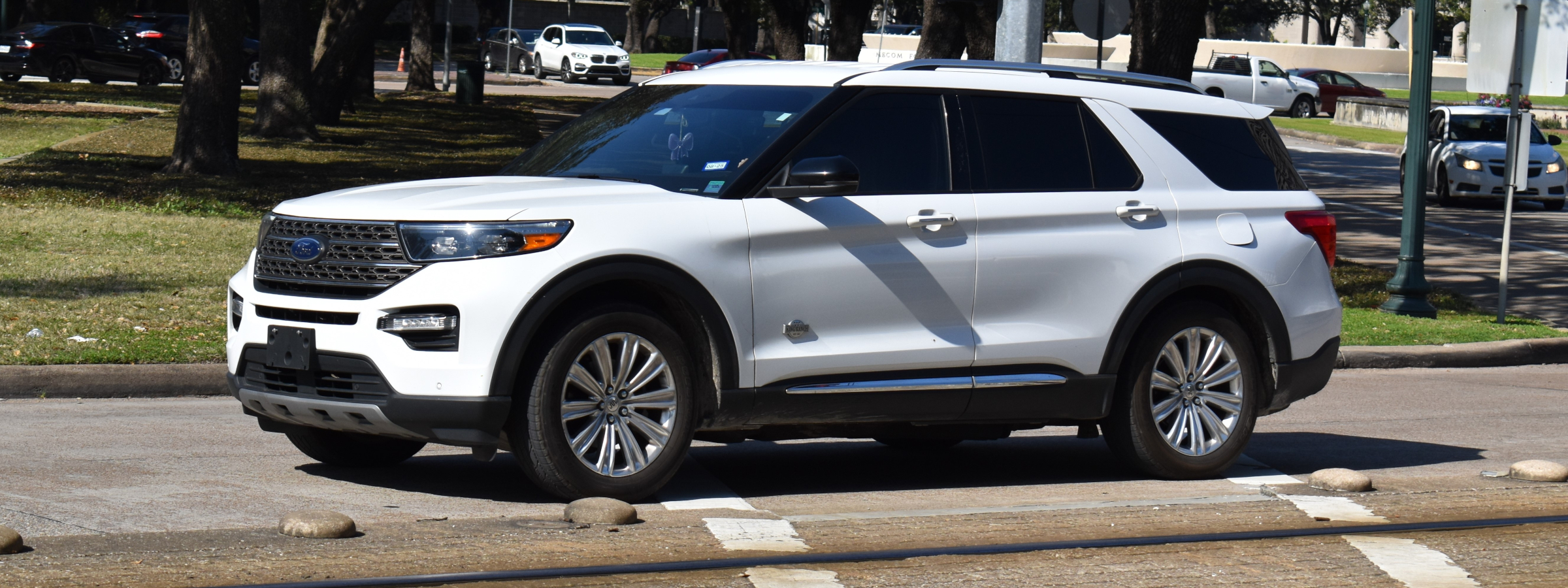 A white Ford Explorer driving past a suburban park.