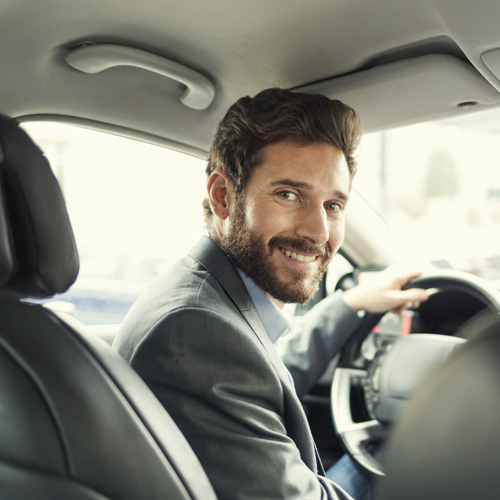 Smiling man in a suit behind the wheel.