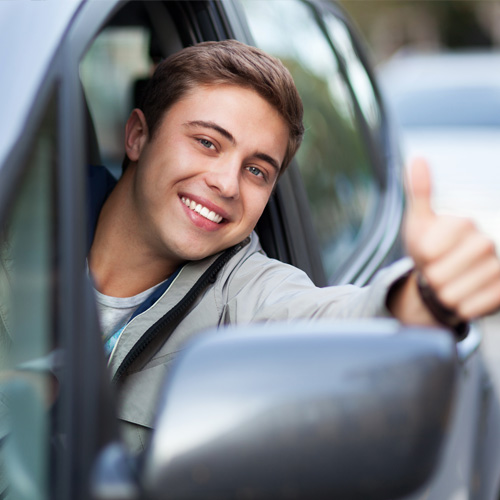 Smiling man leaning out of a car with his thumb up.