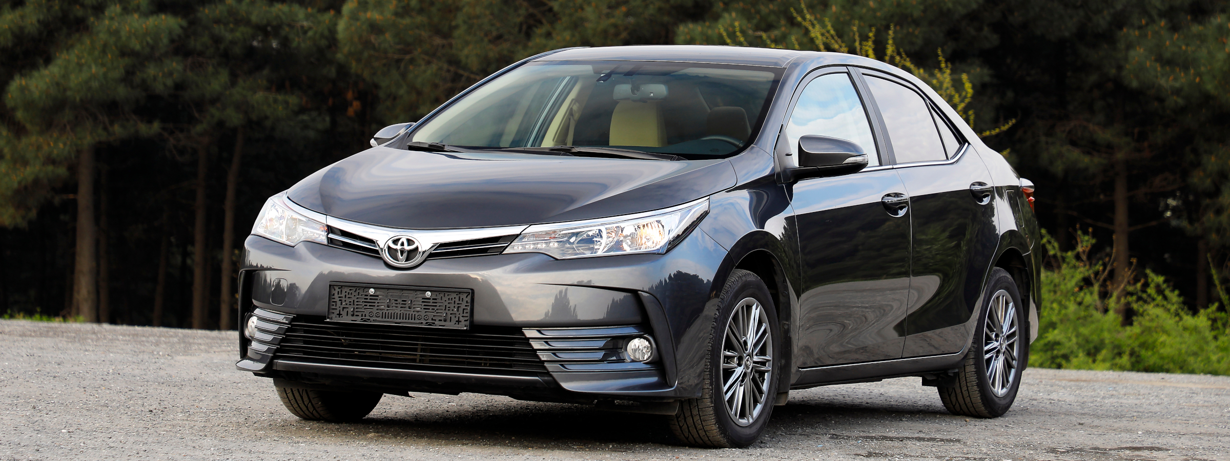 A black Toyota Corolla in front of a wooded area