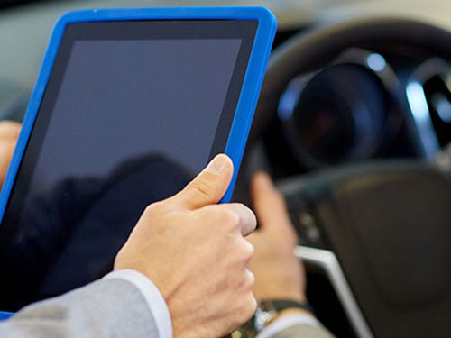 A person holding a tablet while someone is testing a car