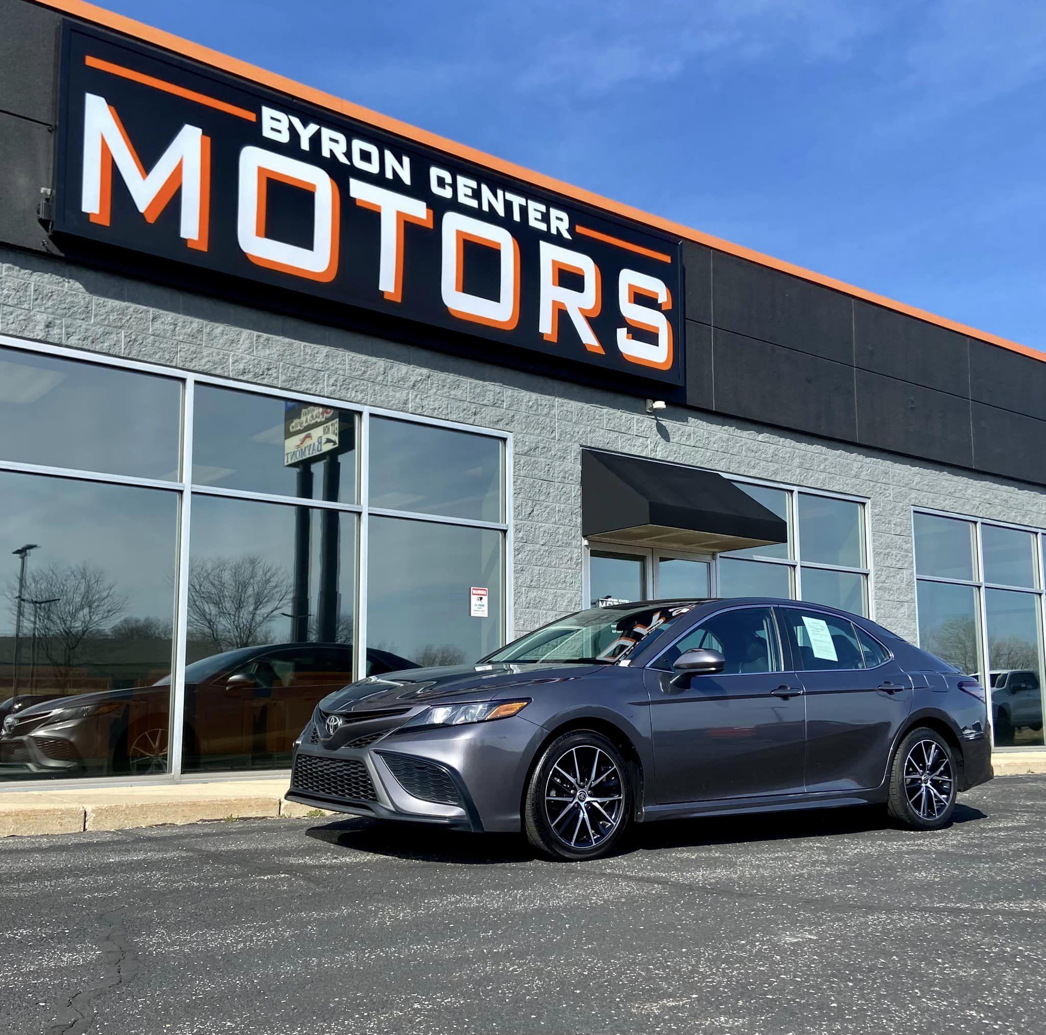 Sedan parked in front of the building with sign in the background for Byron Center Motors used car dealership in Byron Center MI